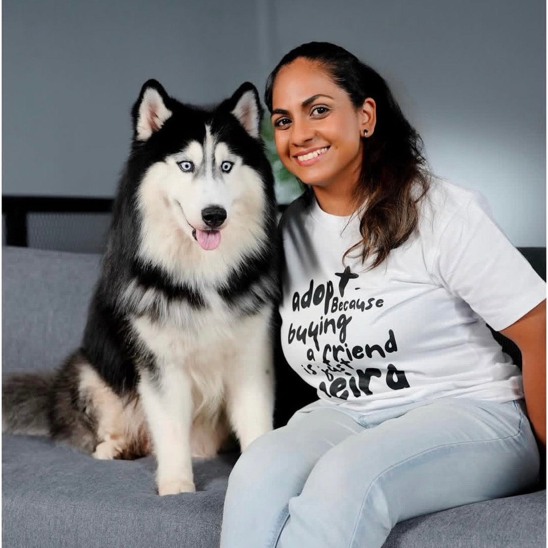 Woman sitting on a couch with a large black and white dog, wearing a white t-shirt with text.