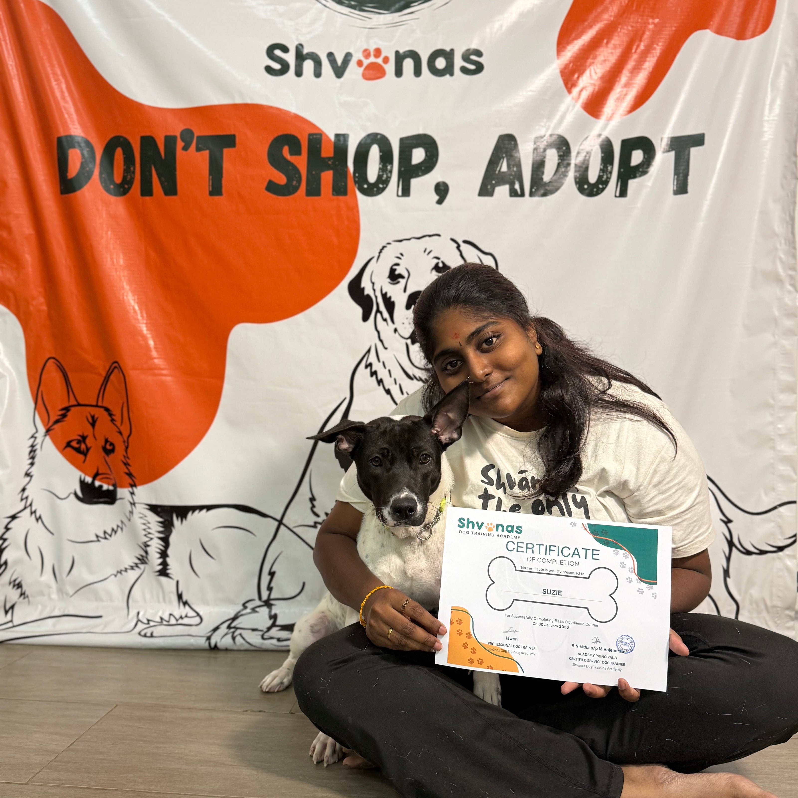 Person holding a dog and a certificate in front of a Shvinas banner with 'Don't Shop, Adopt' text.